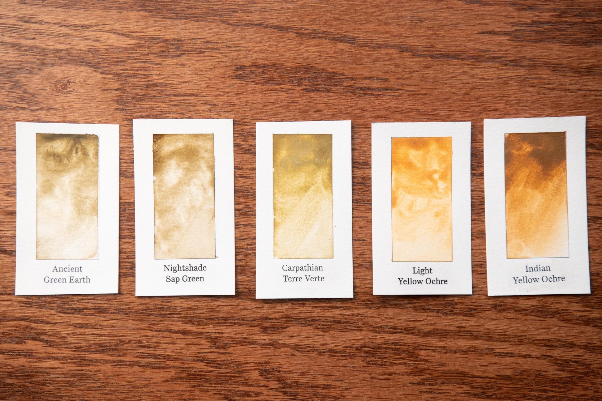 five cards with different shades of yellow, each labeled with a name, arranged on a wooden surface.
