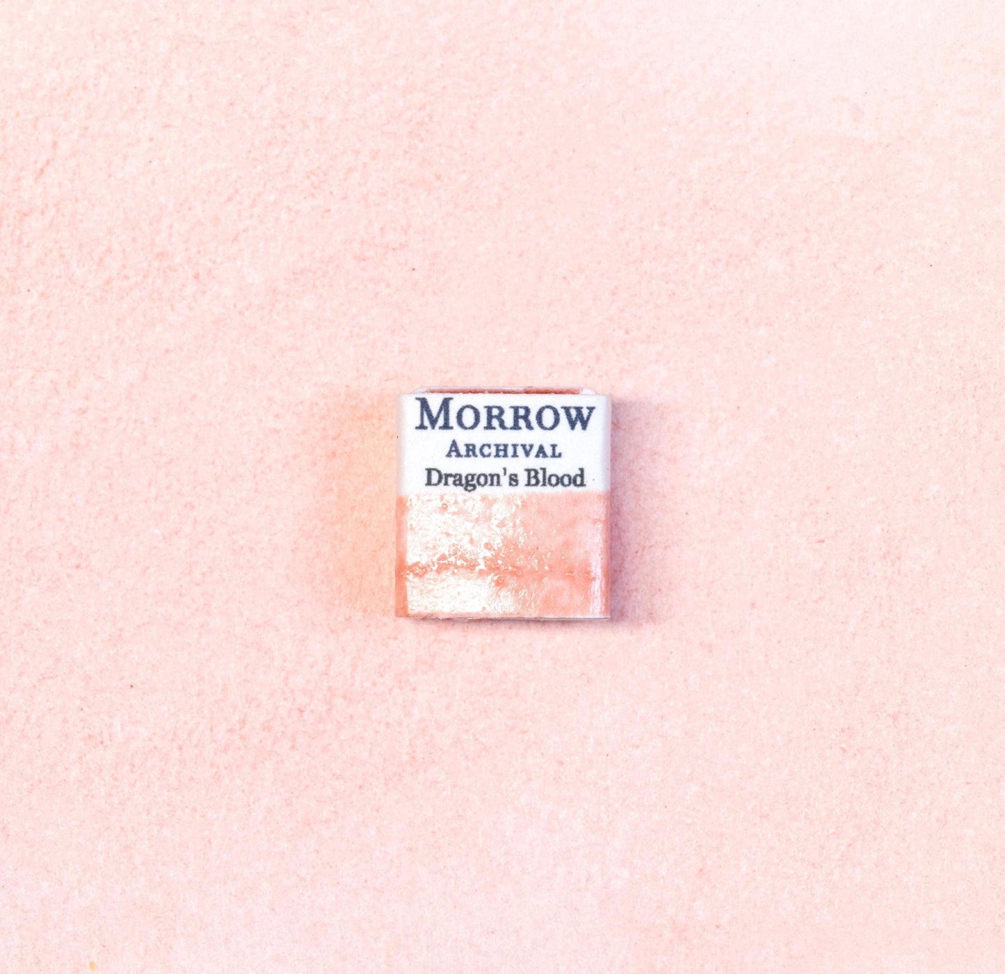 Close-up image of a half pan of Dragon‚Äôs Blood handmade watercolor paint, showing a rich crimson hue with a warm, glowing surface and slight gloss. The pan rests on a neutral background, emphasizing its exotic resin origin and artisanal craftsmanship. Ideal for artists seeking a dramatic, ancient red pigment with mystical associations.