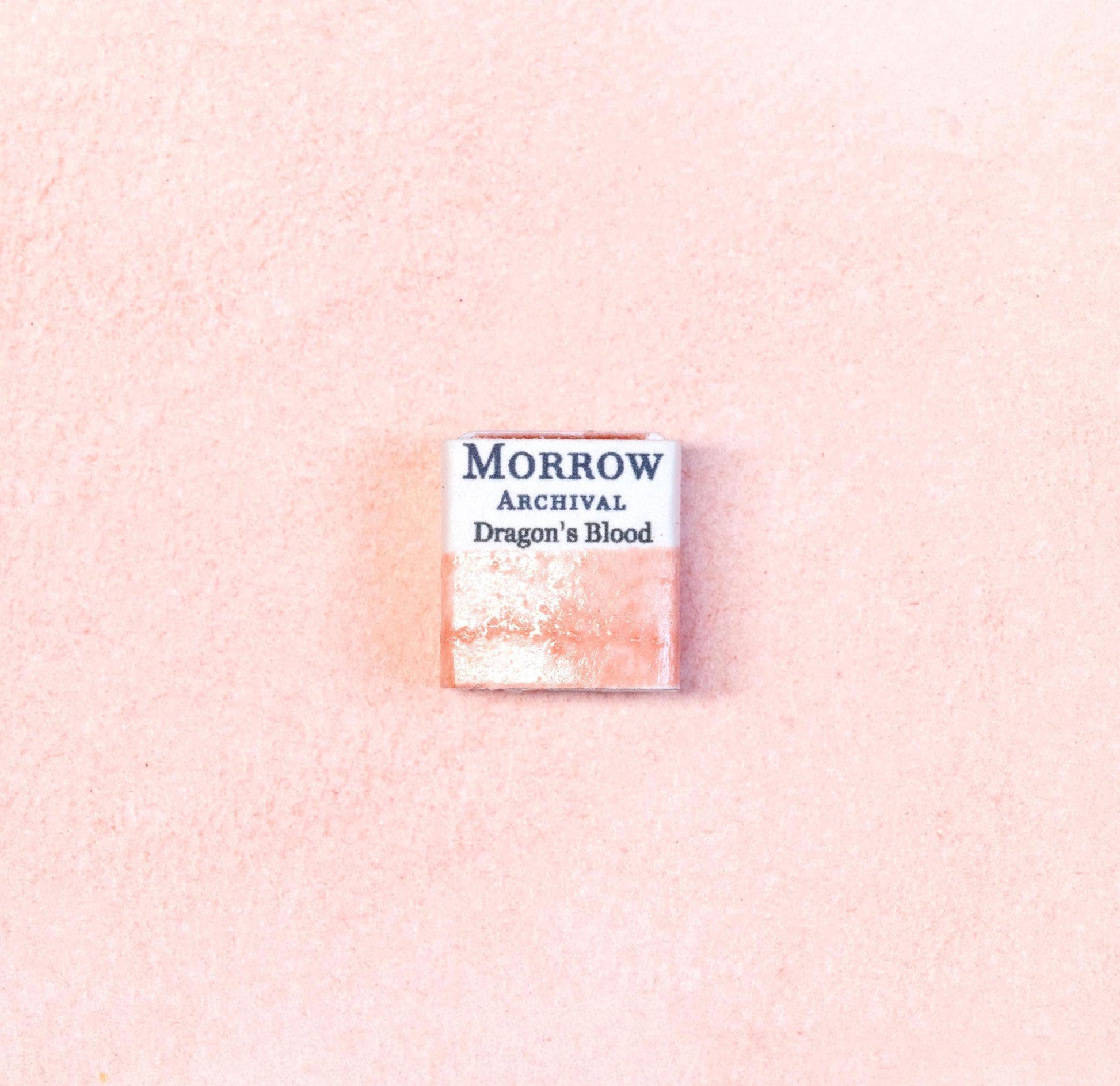 Close-up image of a half pan of Dragon‚Äôs Blood handmade watercolor paint, showing a rich crimson hue with a warm, glowing surface and slight gloss. The pan rests on a neutral background, emphasizing its exotic resin origin and artisanal craftsmanship. Ideal for artists seeking a dramatic, ancient red pigment with mystical associations.