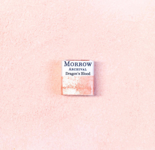 Close-up image of a half pan of Dragon‚Äôs Blood handmade watercolor paint, showing a rich crimson hue with a warm, glowing surface and slight gloss. The pan rests on a neutral background, emphasizing its exotic resin origin and artisanal craftsmanship. Ideal for artists seeking a dramatic, ancient red pigment with mystical associations.