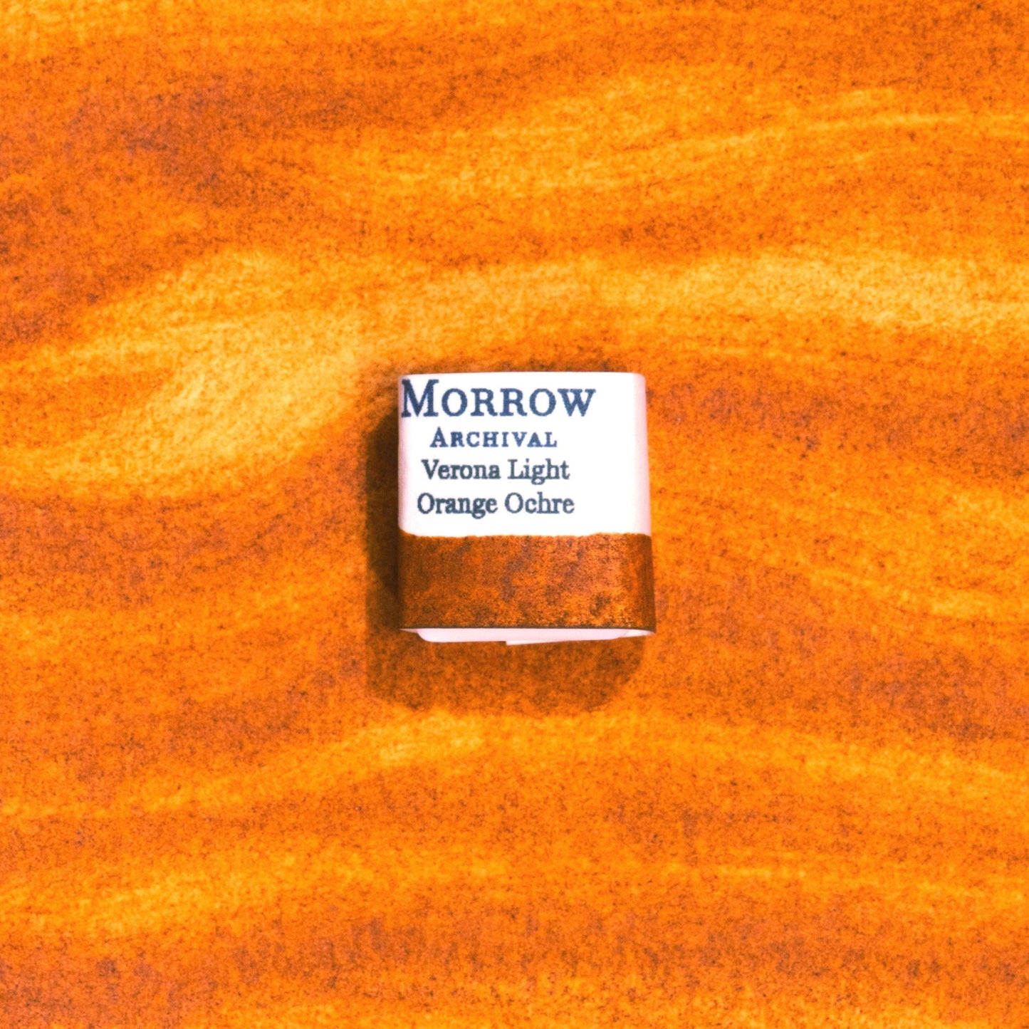 Handmade Verona Orange Ochre natural watercolor paint half pan displayed on a textured watercolor painting. Crafted from pure single-pigment natural earth sourced near Verona, Italy, this warm, earthy orange offers soft granulation and excellent transparency, perfect for botanical illustration, landscape painting, and historical fine art. A beautiful eco-friendly gift for watercolor artists and collectors seeking small-batch, archival-quality, all-natural handmade pigments.