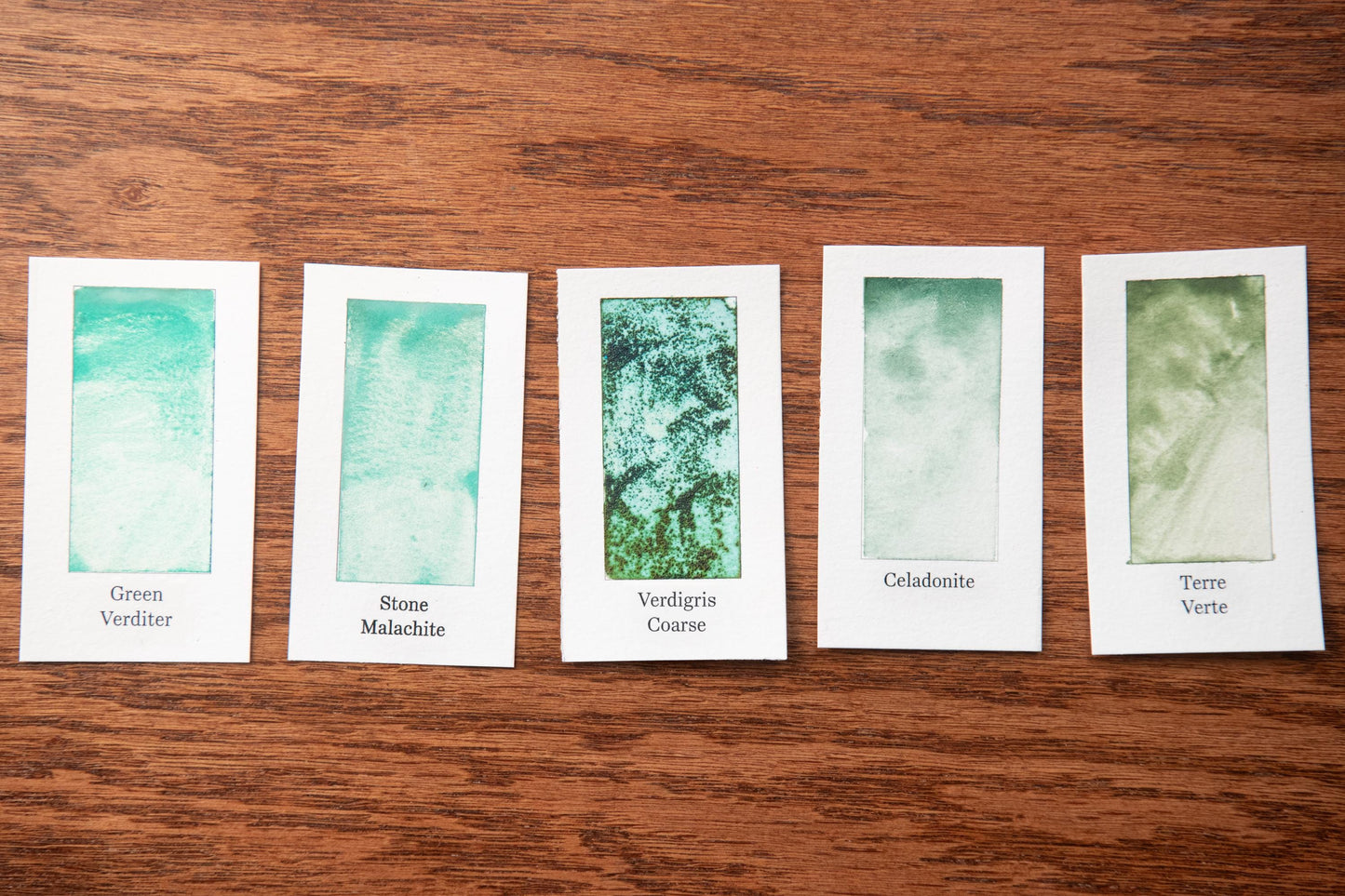 five white cards with different shades of green paint, each labeled with a different type of green paint.