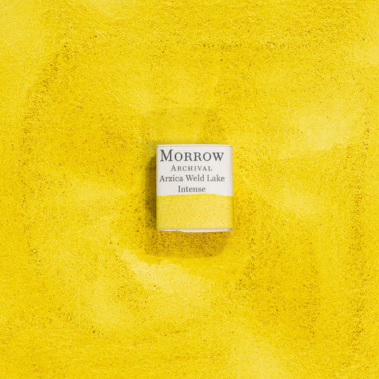 Handmade Arzica Weld Lake Intense Yellow natural watercolor paint half pan shown on a textured watercolor painting. Created from pure single-pigment weld plant extract, this bright, glowing yellow offers excellent transparency and smooth layering, perfect for botanical illustration, historical artwork, and fine art painting. A radiant eco-friendly gift for watercolor artists and collectors seeking small-batch, archival-quality, all-natural handmade pigments with deep historical roots.