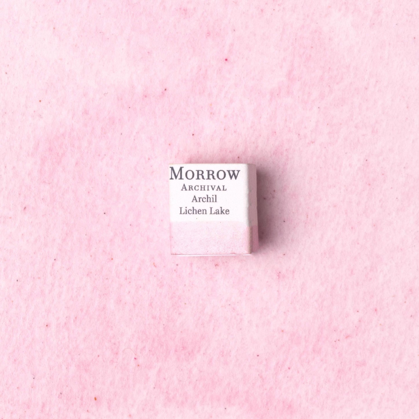 Handmade Archil Lichen Lake Pink natural watercolor paint half pan shown on a textured watercolor painting. Made from pure single-pigment orchil lichen extract, this delicate lavender-pink offers subtle transparency and soft granulation, perfect for botanical art, historical manuscripts, and fine illustration. A rare eco-friendly gift for watercolor artists and collectors seeking small-batch, archival-quality, all-natural handmade pigments with medieval dye origins.