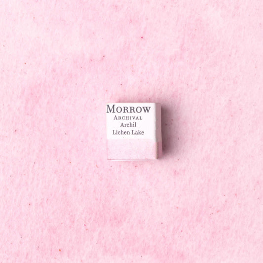 Handmade Archil Lichen Lake Pink natural watercolor paint half pan shown on a textured watercolor painting. Made from pure single-pigment orchil lichen extract, this delicate lavender-pink offers subtle transparency and soft granulation, perfect for botanical art, historical manuscripts, and fine illustration. A rare eco-friendly gift for watercolor artists and collectors seeking small-batch, archival-quality, all-natural handmade pigments with medieval dye origins.