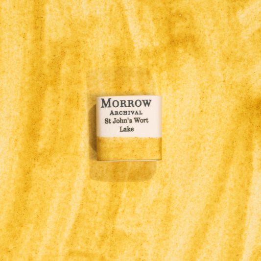 Handmade St. John&#39;s Wort Lake Yellow natural watercolor paint half pan resting on a textured watercolor painting. Made from pure single-pigment St. John&#39;s Wort flowers, this soft, luminous yellow offers delicate transparency and subtle granulation, perfect for botanical painting, historical artwork, and fine illustration. A beautiful eco-friendly gift for watercolor artists and collectors seeking small-batch, archival-quality, all-natural handmade pigments.