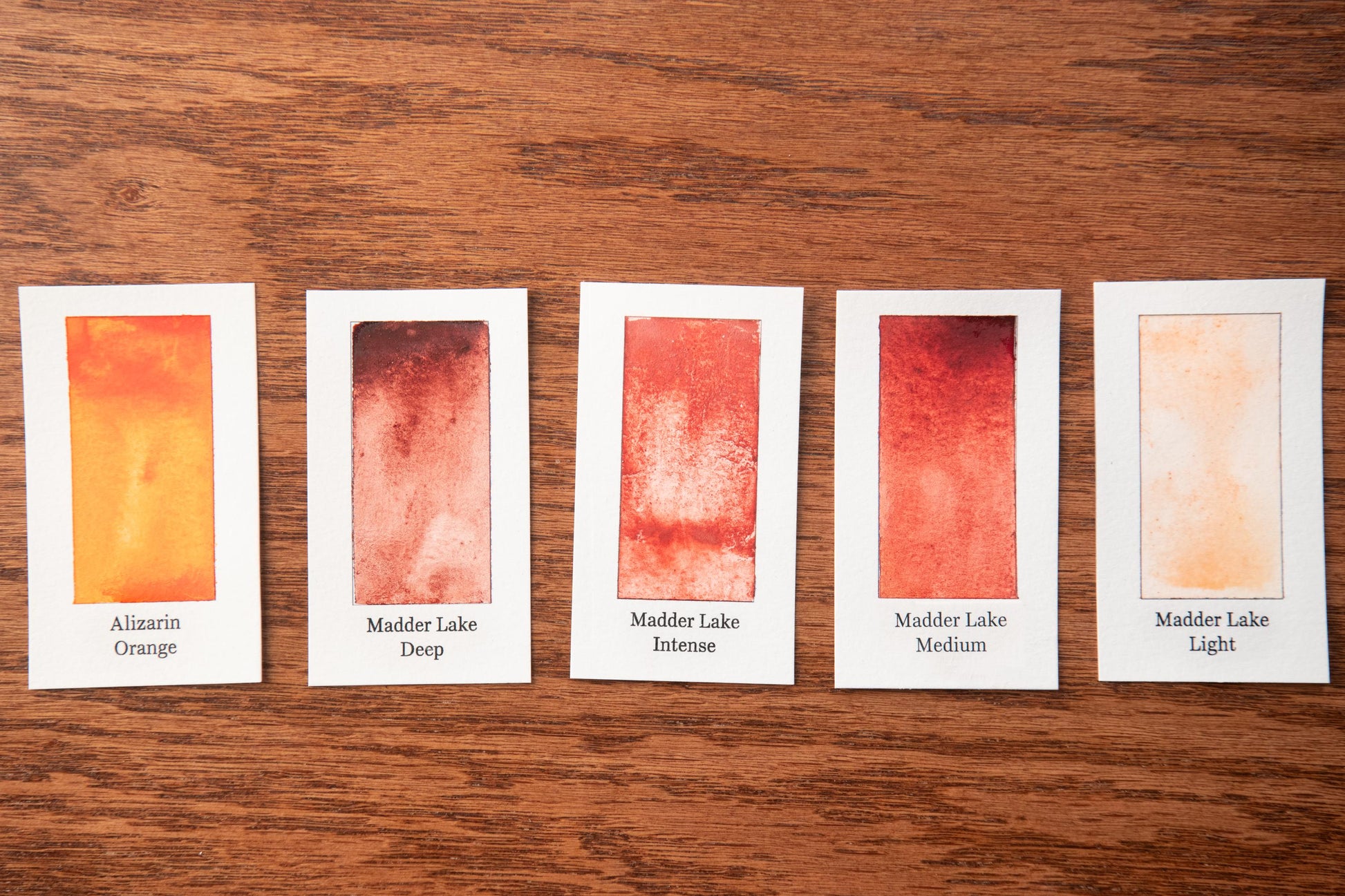 five watercolor paintings with different shades of orange, arranged on a wooden surface.