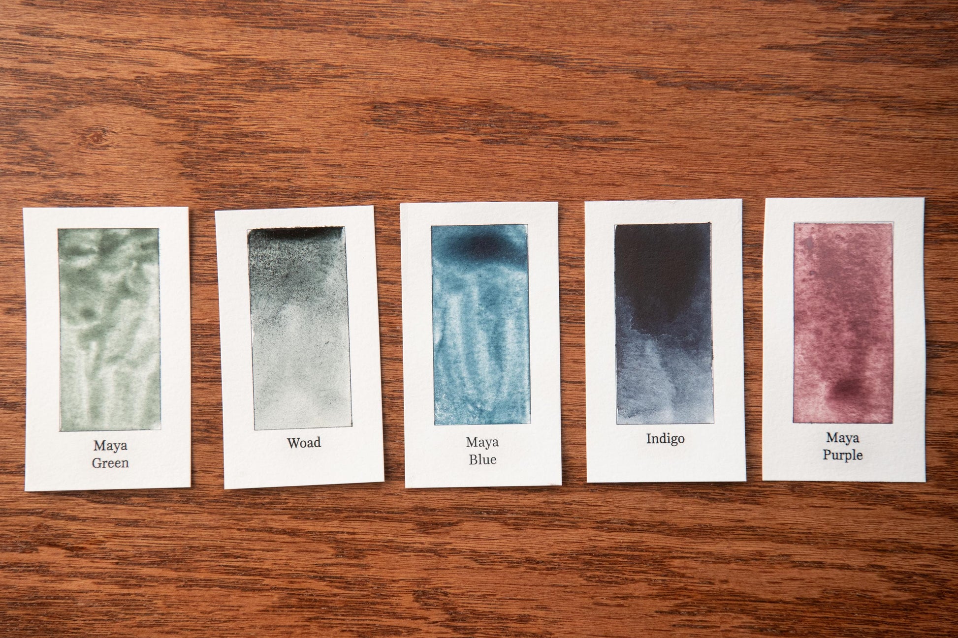 five small art cards with different paint color swatches, arranged on a wooden surface.