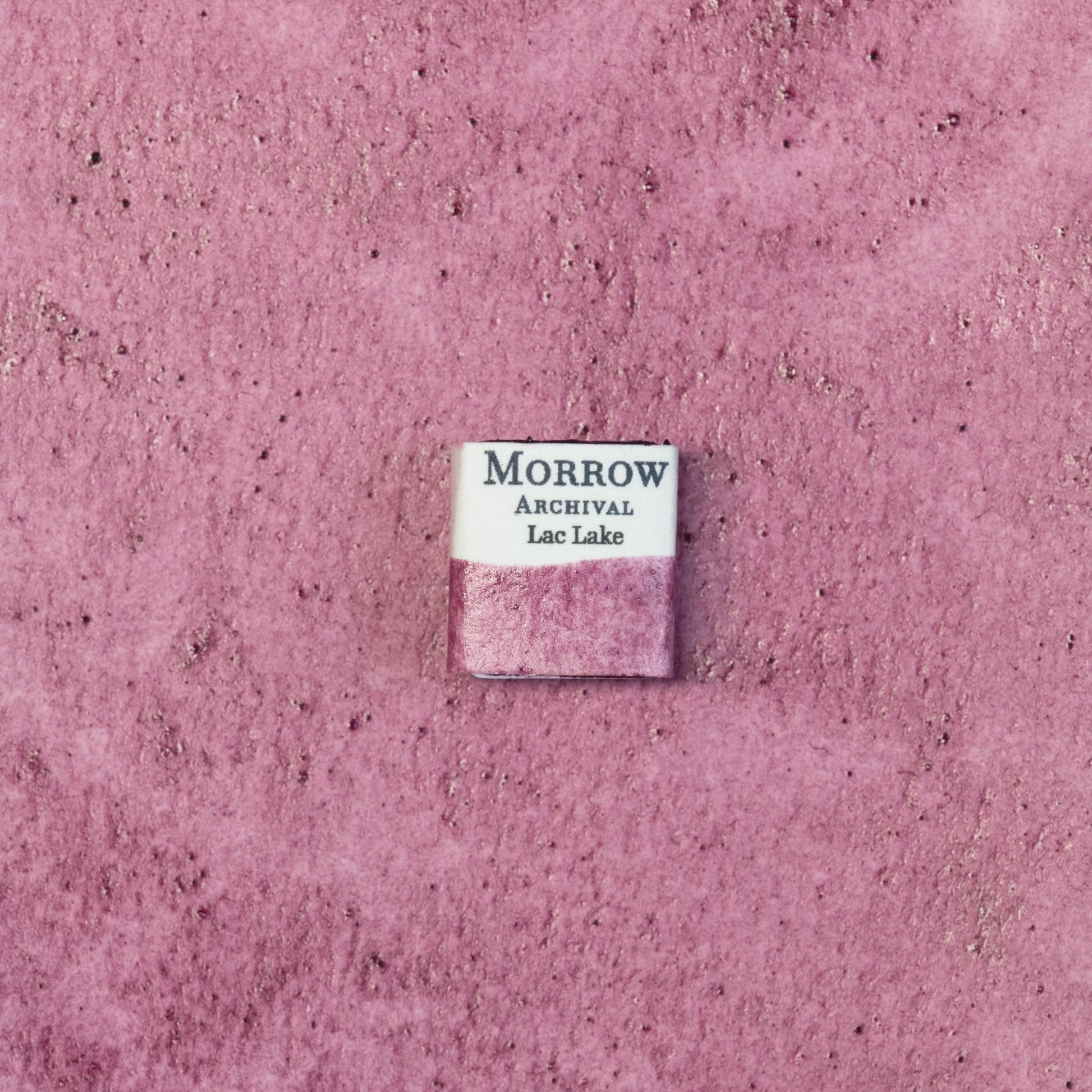 Close-up image of a half pan of Lac Lake Purple handmade watercolor paint, showing a deep magenta-purple hue with a glowing, translucent finish. The pan sits on a neutral background, highlighting its insect-derived origin and refined craftsmanship. Ideal for artists seeking a regal, historical purple with natural botanical warmth.