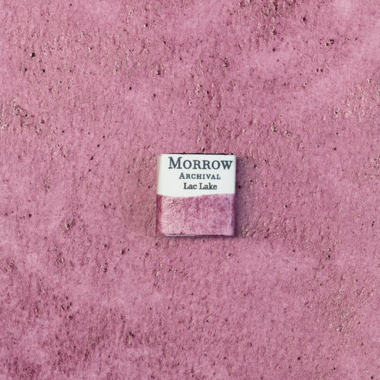 Close-up image of a half pan of Lac Lake Purple handmade watercolor paint, showing a deep magenta-purple hue with a glowing, translucent finish. The pan sits on a neutral background, highlighting its insect-derived origin and refined craftsmanship. Ideal for artists seeking a regal, historical purple with natural botanical warmth.