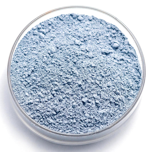 A glass container filled with a blue-gray powder substance, possibly a chemical or industrial ingredient.