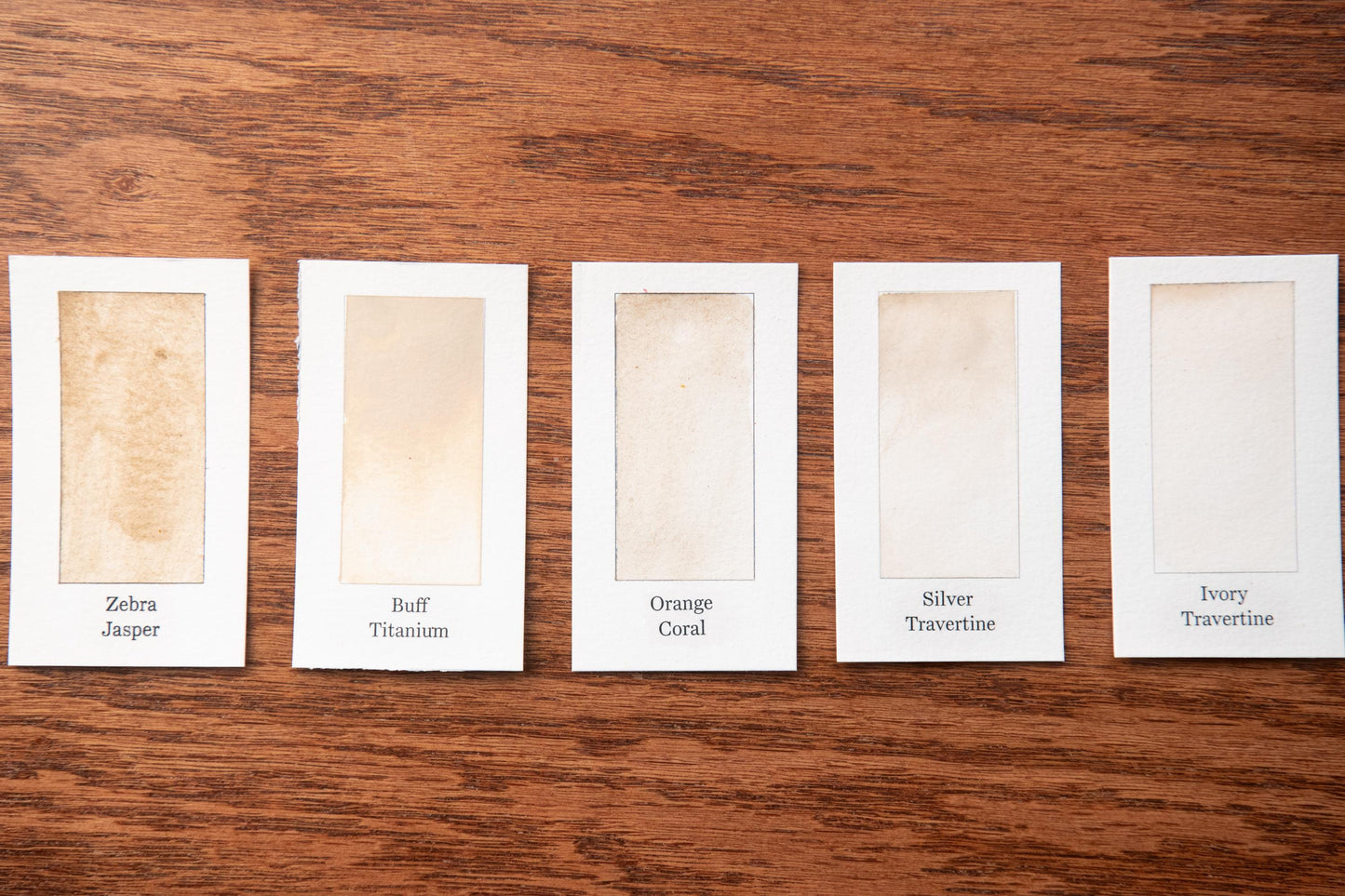 five white cards with different shades of beige, arranged on a wooden surface.