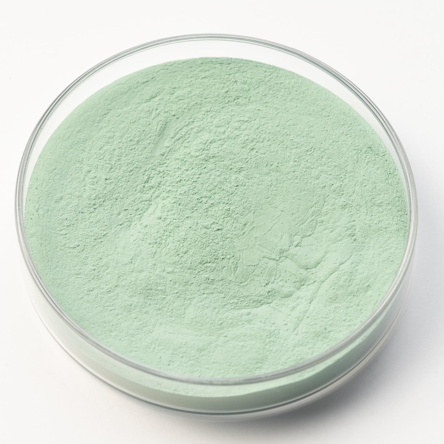 A clear glass petri dish containing Victoria Green Pigment, a fine light green powder, is displayed on a white background.