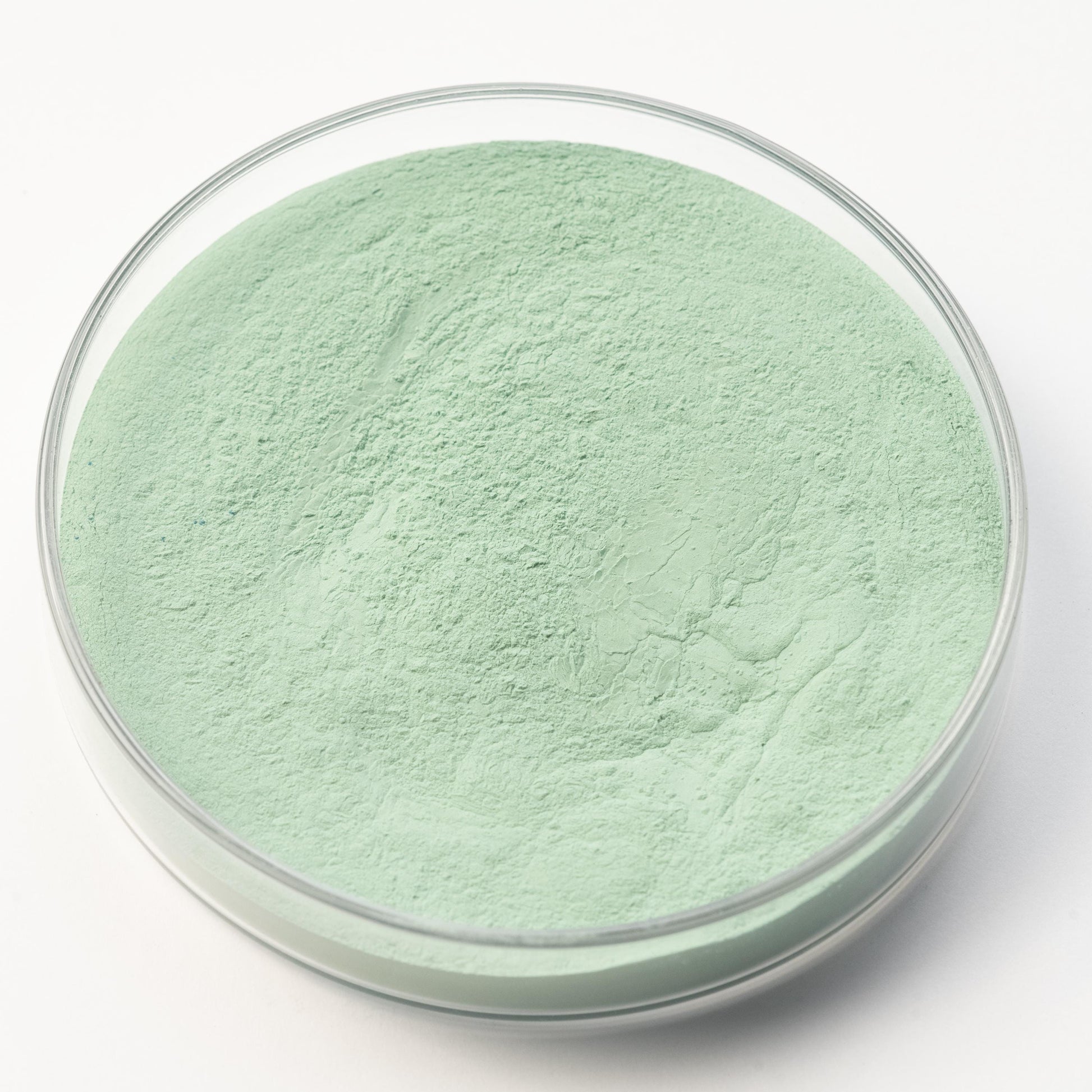A clear glass petri dish containing Victoria Green Pigment, a fine light green powder, is displayed on a white background.