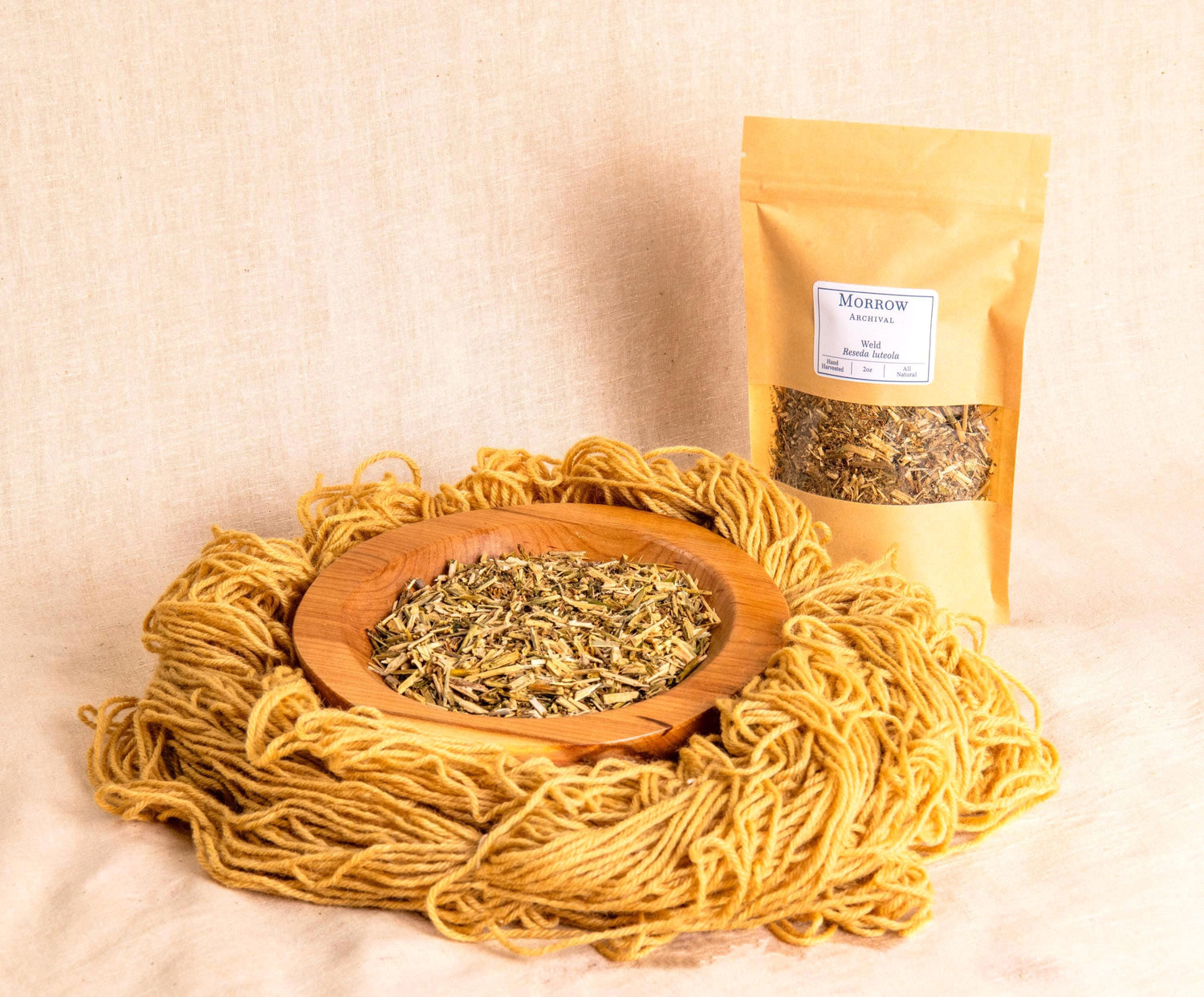 Weld Dye by Morrow Archival, shown as a soft yellow powder in a wooden bowl, alongside brilliant yellow-dyed wool yarn and a labeled kraft pouch. Derived from Reseda luteola, one of the oldest known yellow dye plants, weld produces clear, lightfast yellows used in medieval European tapestries and botanical dye traditions. Perfect for natural dyeing, historic reproduction, and sustainable fiber arts seeking luminous plant-based color.