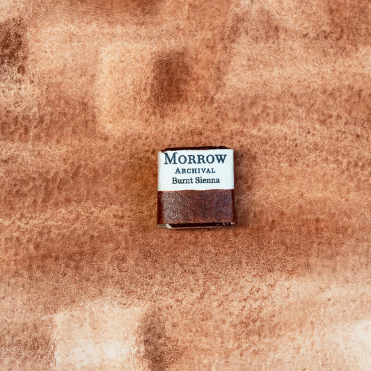 Close-up image of a half pan of Burnt Sienna handmade watercolor paint, featuring a deep reddish-brown hue with a matte finish and soft granulation. The pan sits on a neutral background, highlighting its natural clay origin and artisanal, small-batch craftsmanship. Ideal for artists seeking a warm, classic earth tone for shadows, portraits, and naturalistic work.