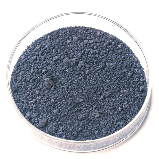 A glass container filled with dark, granular material, possibly a type of soil or mineral.