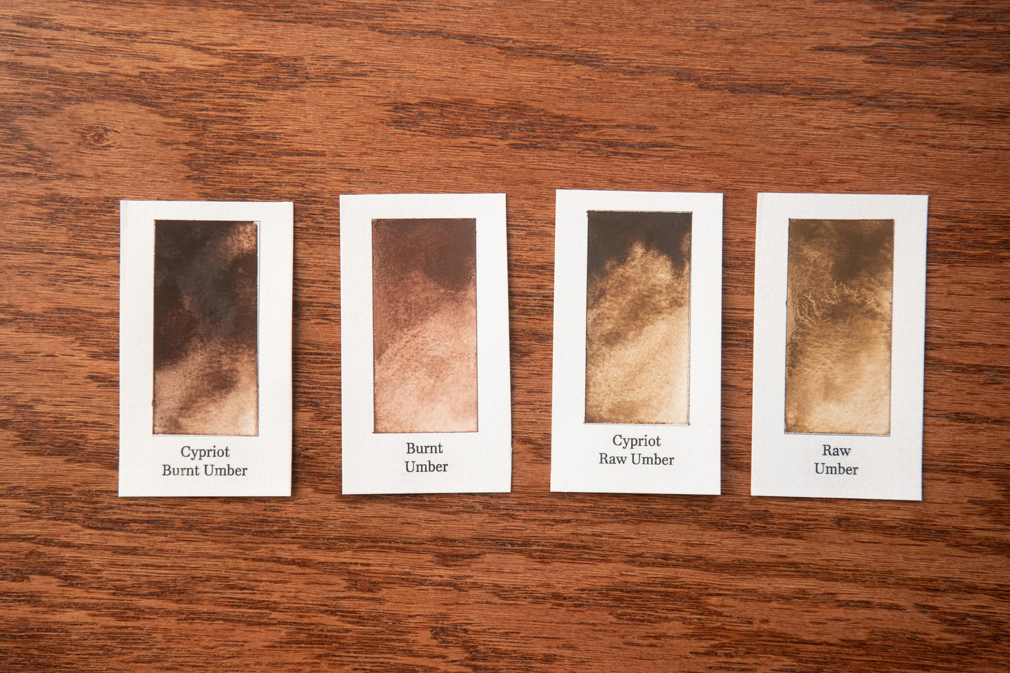 four identical cards with different shades of brown, arranged on a wooden surface.