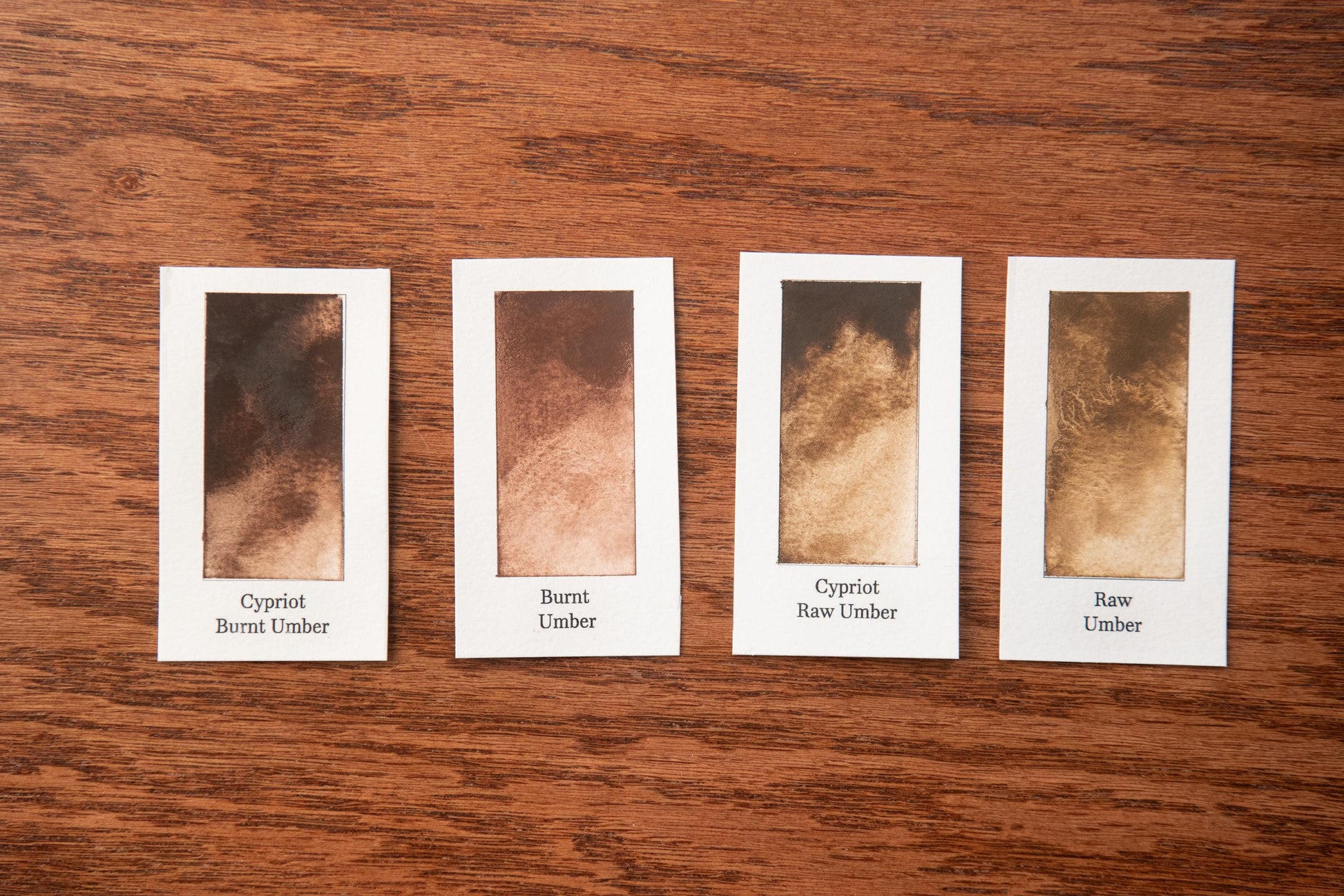 four identical cards with different shades of brown, arranged on a wooden surface.