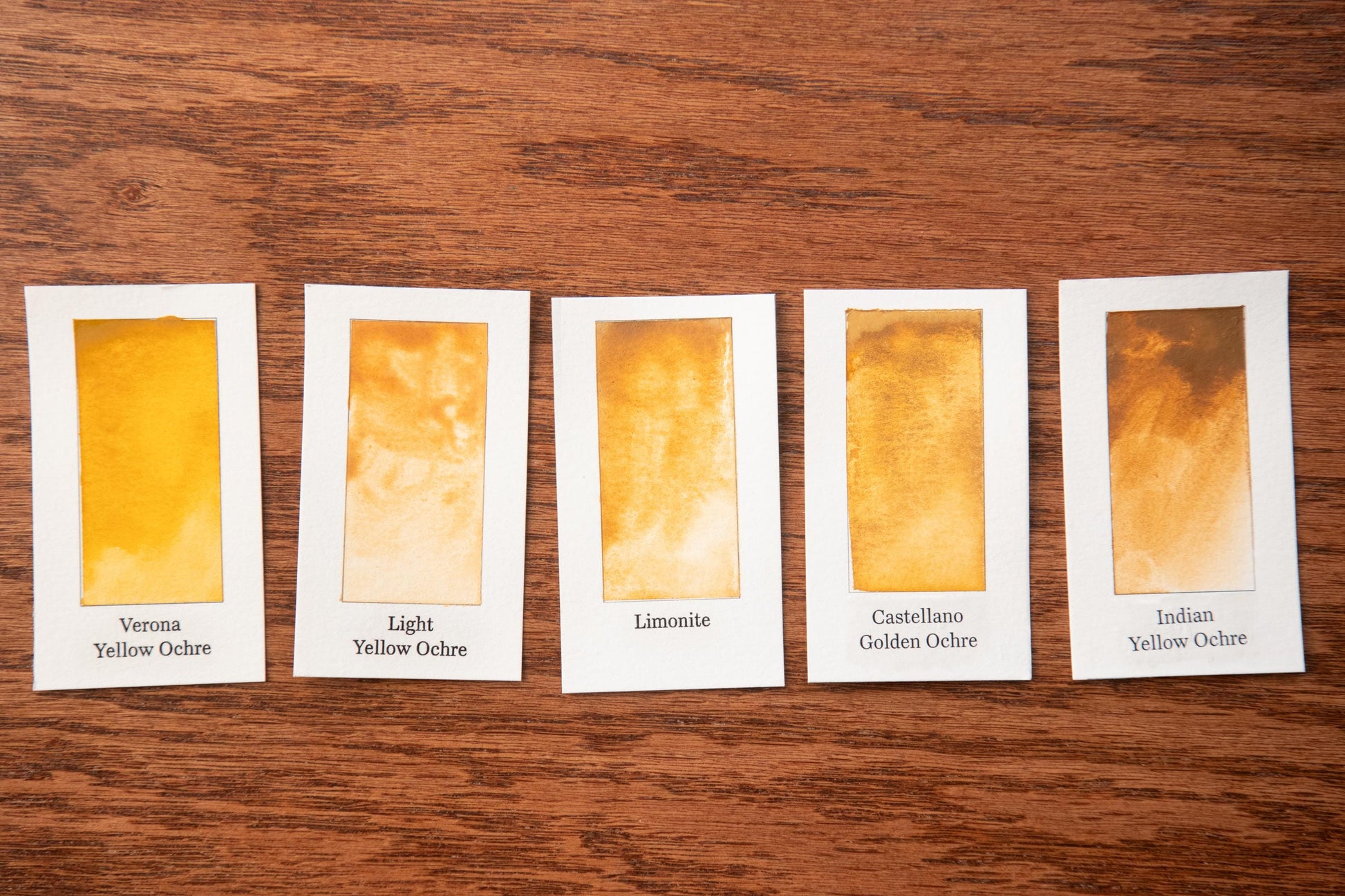 five small cards with different shades of yellow ochre, arranged on a wooden surface.