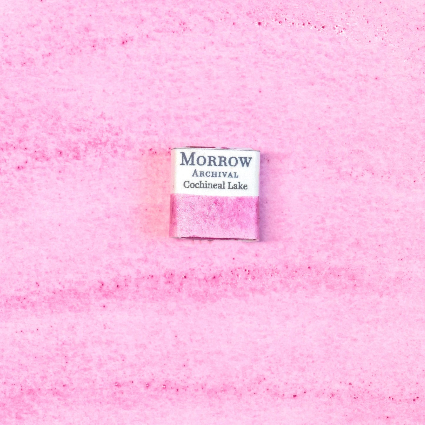 Close-up image of a half pan of Cochineal Lake handmade watercolor paint, featuring a vibrant crimson-pink hue with a glowing, translucent finish. The pan rests on a neutral background, highlighting the pigment‚Äôs insect-derived origin and traditional craftsmanship. Ideal for artists seeking a historically accurate, warm red with deep cultural roots and natural brilliance.