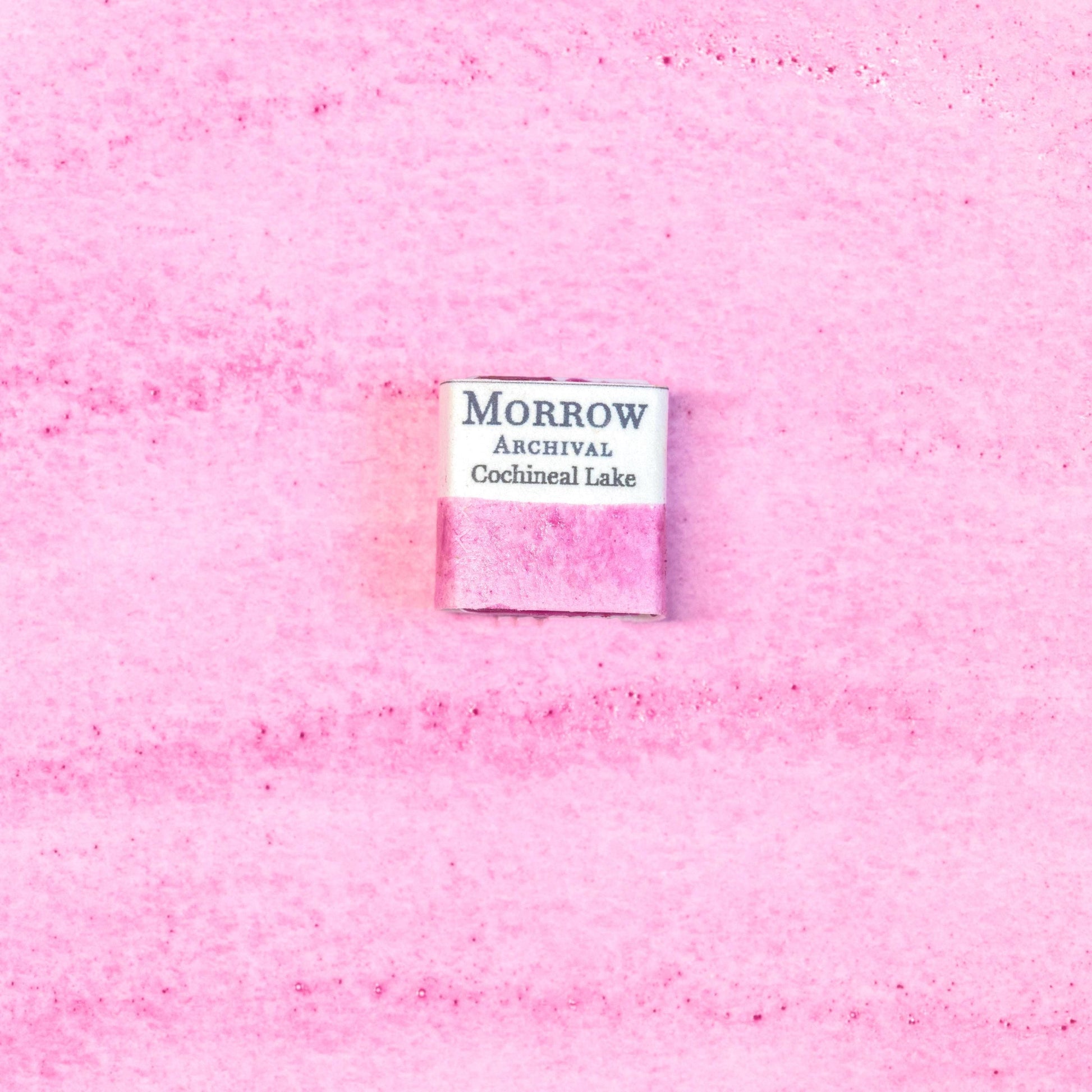 Close-up image of a half pan of Cochineal Lake handmade watercolor paint, featuring a vibrant crimson-pink hue with a glowing, translucent finish. The pan rests on a neutral background, highlighting the pigment‚Äôs insect-derived origin and traditional craftsmanship. Ideal for artists seeking a historically accurate, warm red with deep cultural roots and natural brilliance.