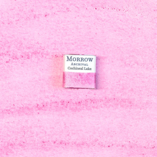 Close-up image of a half pan of Cochineal Lake handmade watercolor paint, featuring a vibrant crimson-pink hue with a glowing, translucent finish. The pan rests on a neutral background, highlighting the pigment‚Äôs insect-derived origin and traditional craftsmanship. Ideal for artists seeking a historically accurate, warm red with deep cultural roots and natural brilliance.