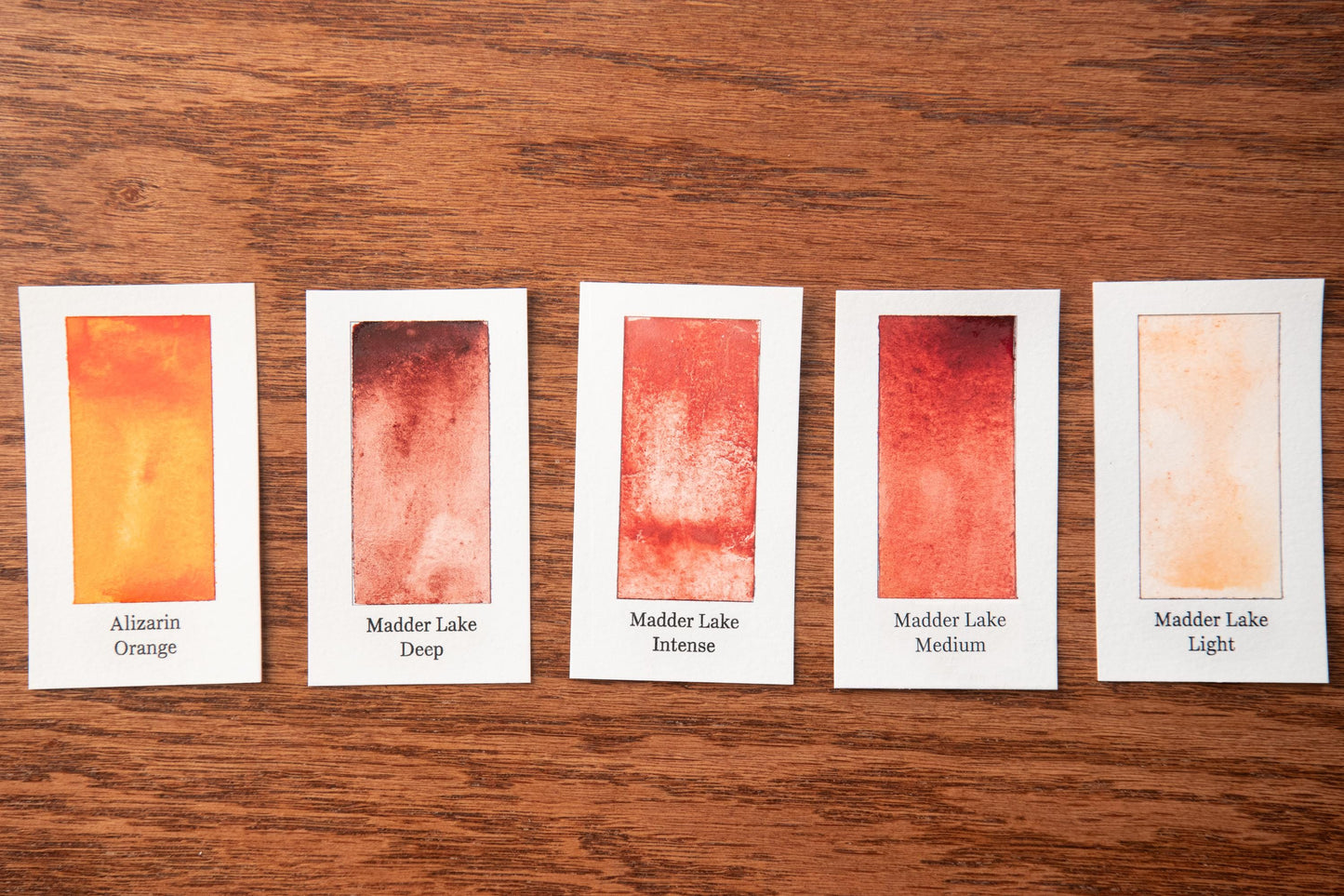 five watercolor paintings with different shades of orange, arranged on a wooden surface.