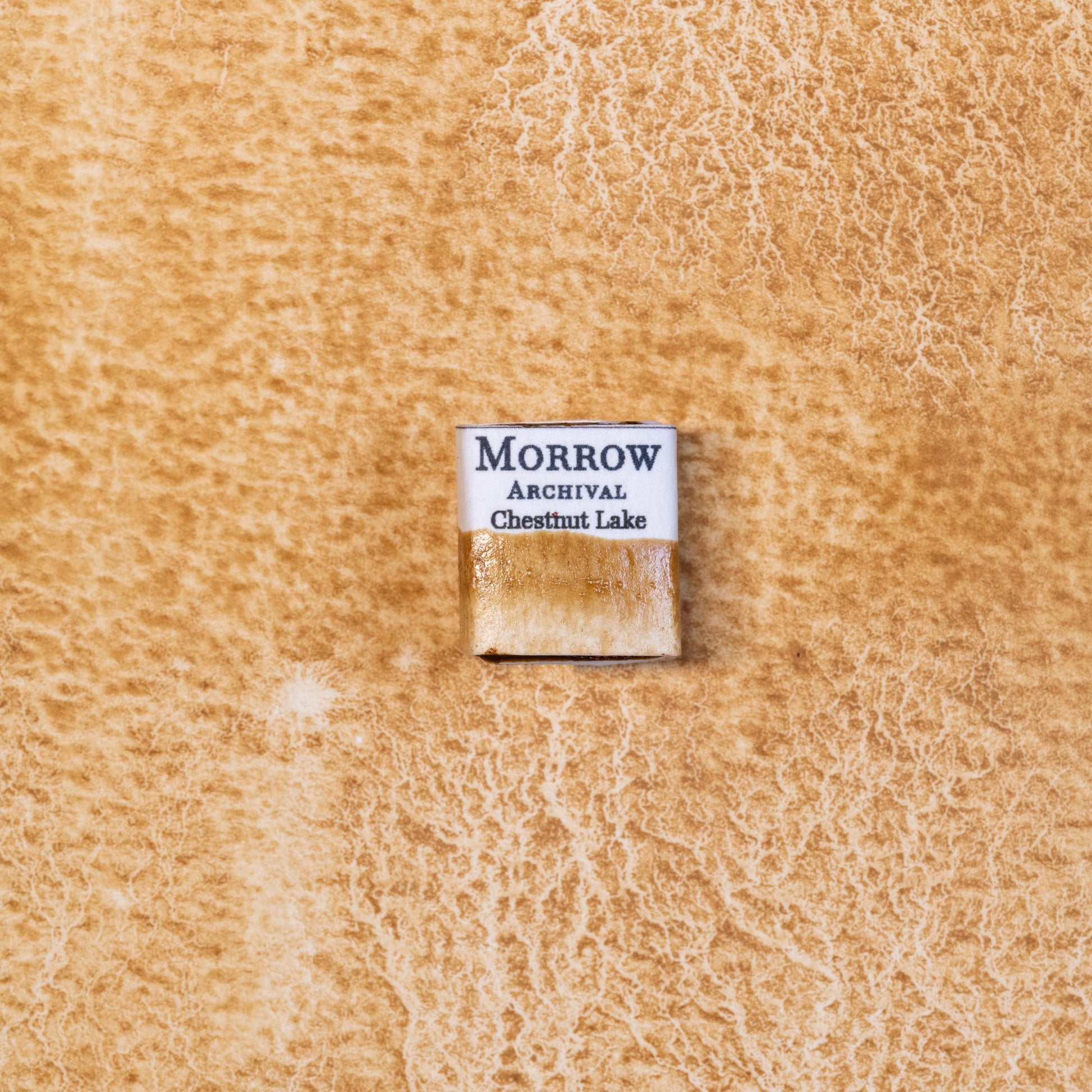 Close-up image of a half pan of Chestnut Lake handmade watercolor paint, featuring a warm, natural brown hue with soft amber undertones and a smooth, matte surface. The pan rests on a neutral background, highlighting its botanical source and artisanal, small-batch craftsmanship. Ideal for artists seeking a plant-based historic brown with gentle character.