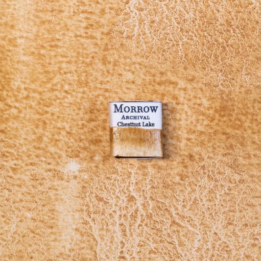 Close-up image of a half pan of Chestnut Lake handmade watercolor paint, featuring a warm, natural brown hue with soft amber undertones and a smooth, matte surface. The pan rests on a neutral background, highlighting its botanical source and artisanal, small-batch craftsmanship. Ideal for artists seeking a plant-based historic brown with gentle character.