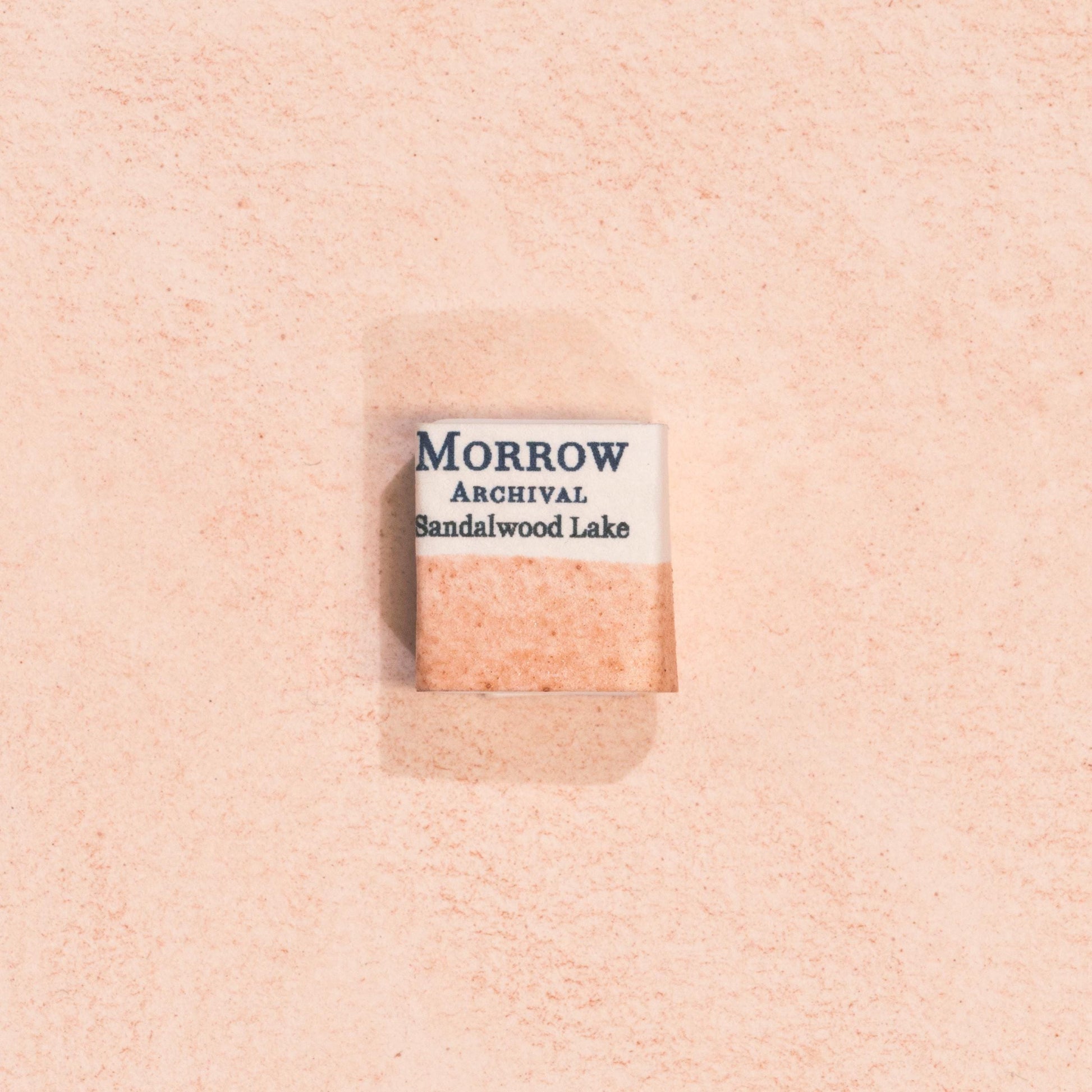 Handmade Sandalwood Lake Pink natural watercolor paint half pan displayed on a textured watercolor painting. Created from pure single-pigment sandalwood extract, this soft, warm pink offers gentle transparency and smooth granulation, ideal for botanical illustration, historical artwork, and fine art painting. A perfect eco-friendly gift for watercolor artists, nature lovers, and collectors seeking small-batch, archival-quality, all-natural handmade pigments.