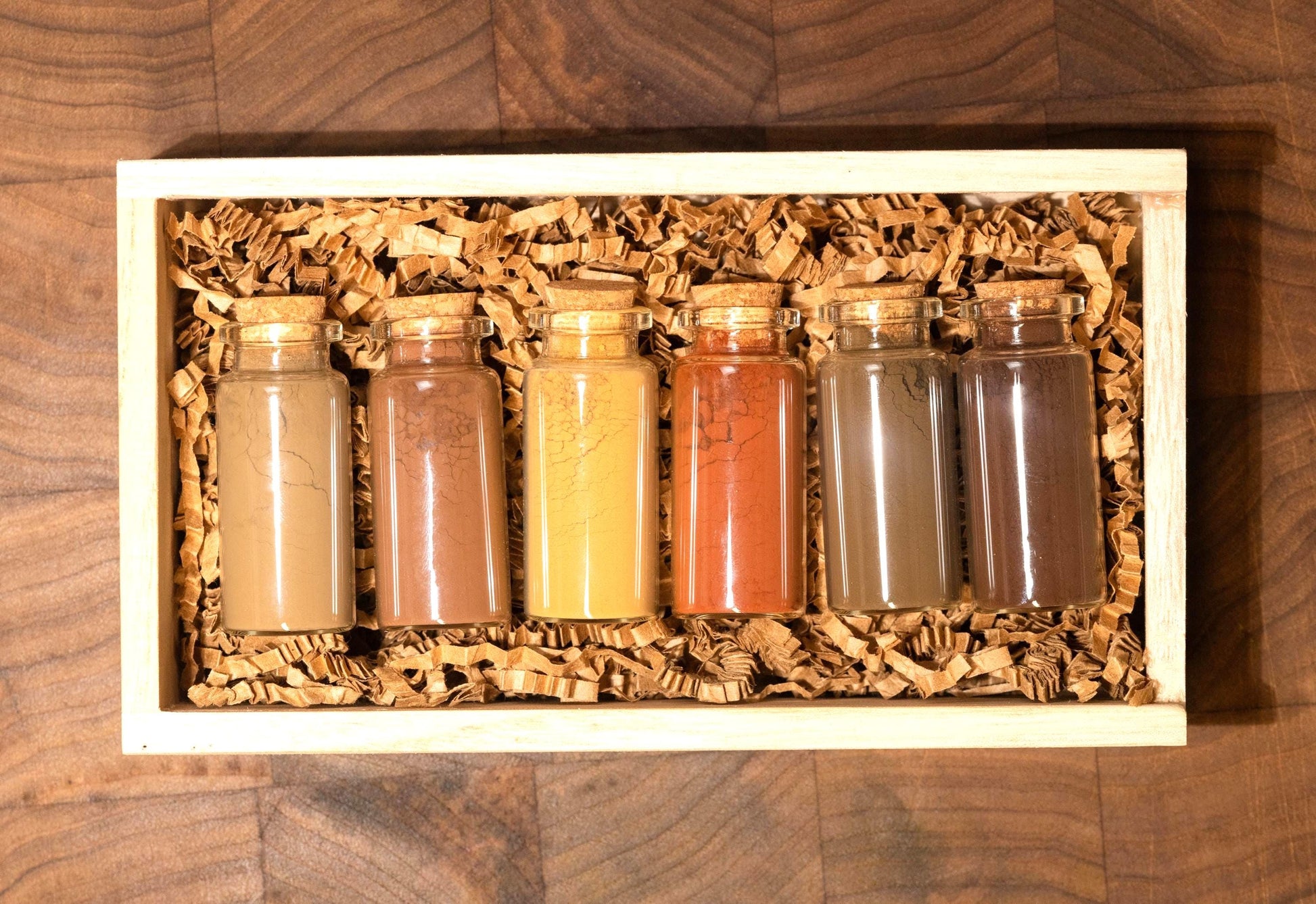 Set of 6 all natural ochre earth pigments in 1oz glass bottles with corks, nestled in shredded recycled kraft paper inside a handcrafted wooden gift box. Resting on a dark walnut wood board with soft, moody lighting, this all-natural artist gift set is ideal for birthdays, holidays, or creative milestones. Each bottle contains rich earth pigments in tones from golden yellow to deep green and warm brown as well as red and orange and are archival quality and lightfast for painting.