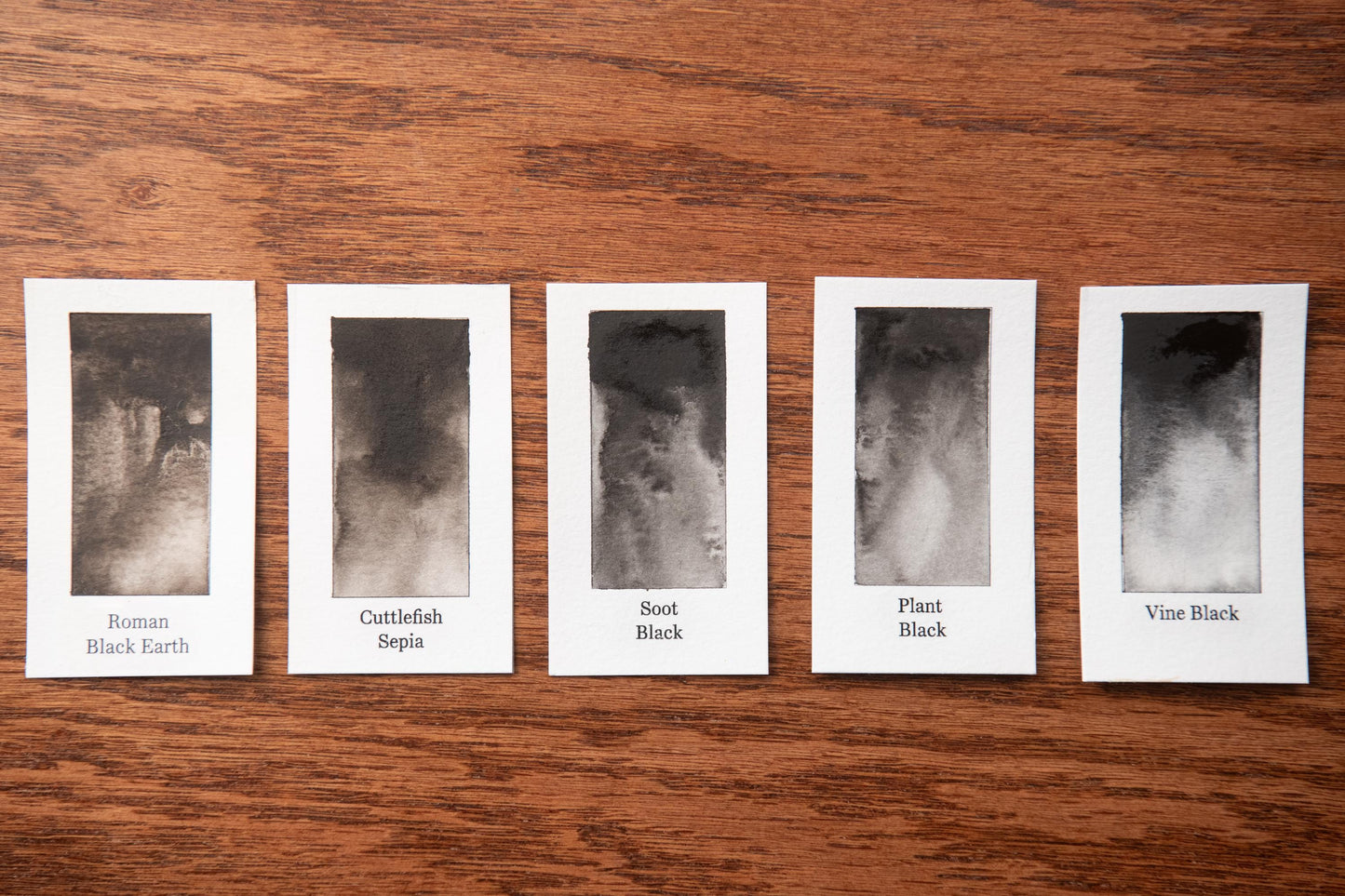 five black and white photographs arranged in a row on a wooden surface, each labeled with a different color.