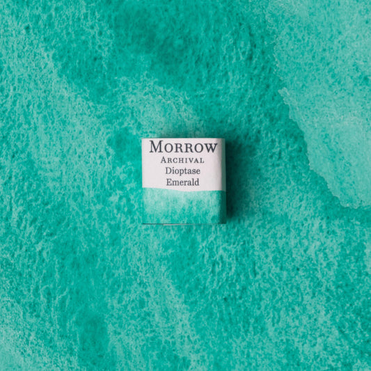 Handmade Emerald Dioptase natural watercolor paint half pan resting on a textured watercolor painting. Made from pure single-pigment dioptase crystal, this brilliant emerald green offers intense color, dramatic granulation, and a natural mineral shimmer‚Äîideal for botanical art, gemstone studies, and historical illustration. A rare eco-friendly gift for watercolor artists and collectors seeking small-batch, archival-quality, all-natural handmade pigments with geological elegance.