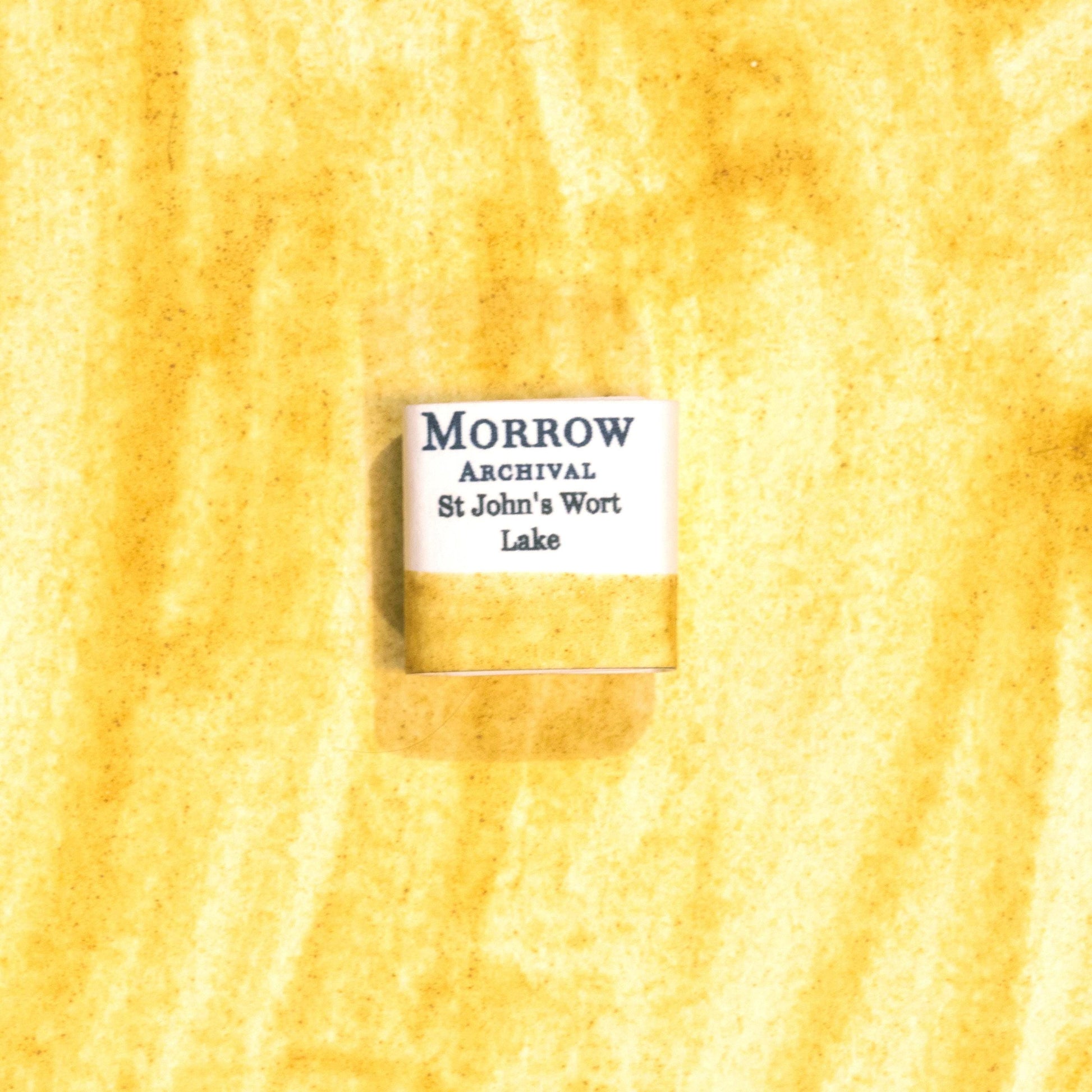 Handmade St. John's Wort Lake Yellow natural watercolor paint half pan resting on a textured watercolor painting. Made from pure single-pigment St. John's Wort flowers, this soft, luminous yellow offers delicate transparency and subtle granulation, perfect for botanical painting, historical artwork, and fine illustration. A beautiful eco-friendly gift for watercolor artists and collectors seeking small-batch, archival-quality, all-natural handmade pigments.