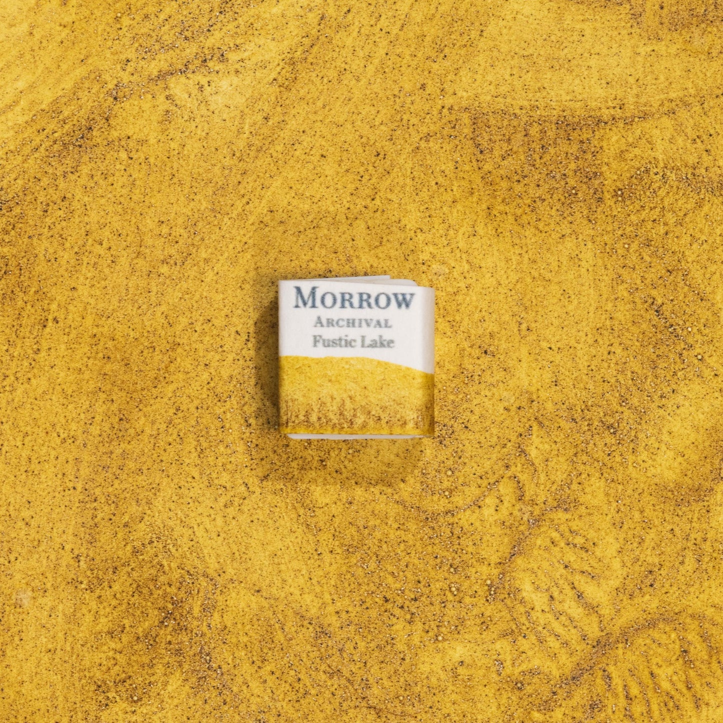 Handmade Fustic Lake Deep Yellow natural watercolor paint half pan shown on a textured watercolor painting. Crafted from pure single-pigment fustic wood extract, this rich golden yellow offers warm transparency and soft granulation, perfect for botanical painting, historical illustration, and naturalist art. A beautiful eco-friendly gift for watercolor artists and collectors seeking small-batch, archival-quality, all-natural handmade pigments with a deep historical legacy.