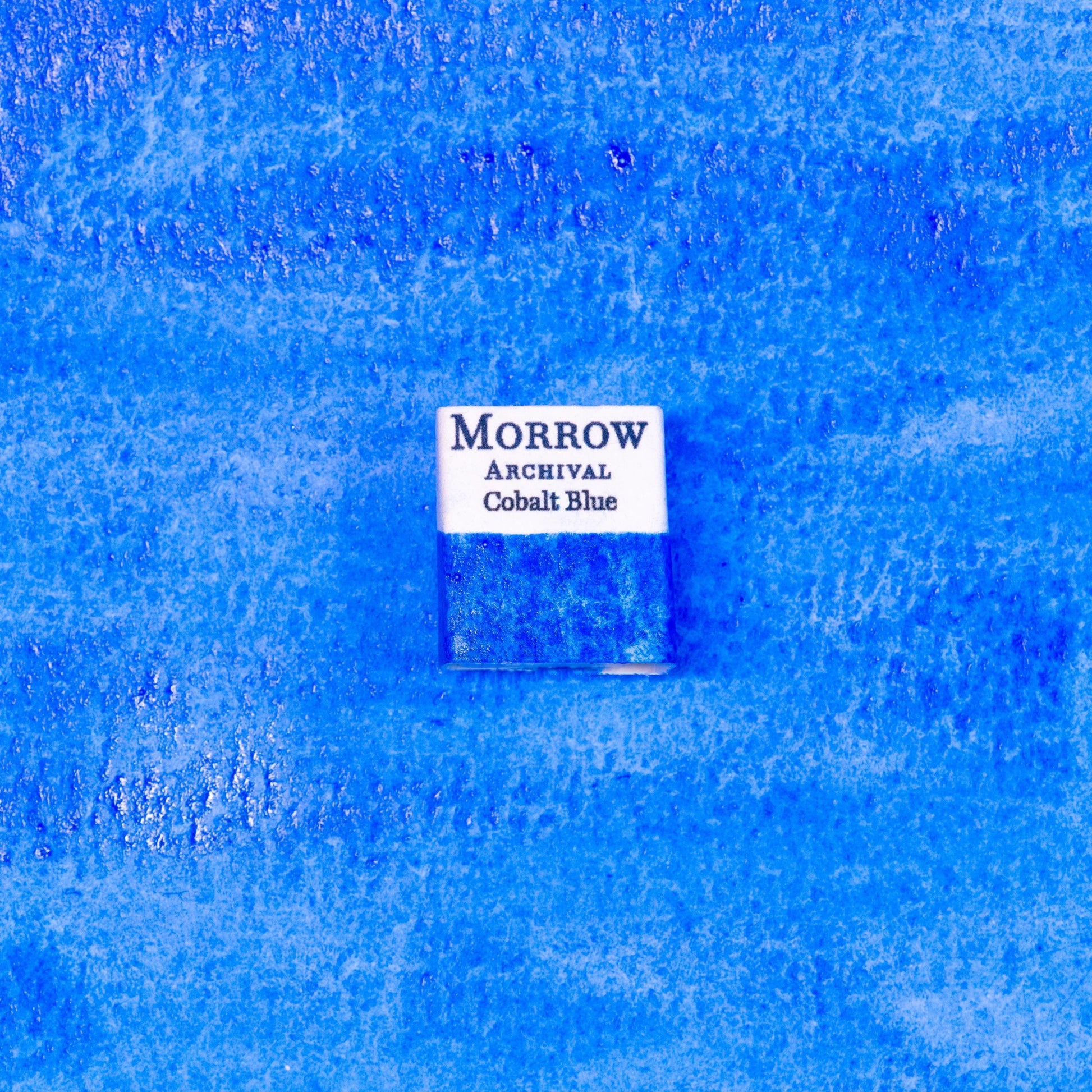 Close-up image of a half pan of Cobalt Blue handmade watercolor paint, showing a vivid, sky-blue hue with subtle granulation and a velvety matte surface. The pan sits on a neutral background, emphasizing its mineral origin and artisanal craftsmanship. Ideal for artists seeking a cool, luminous blue with historic depth and professional performance.