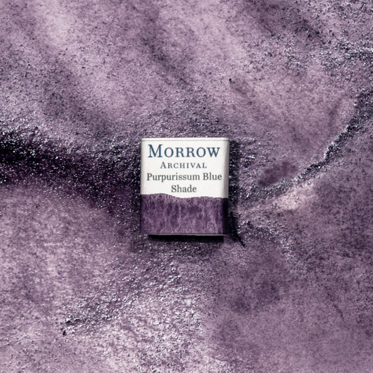 Close-up image of a half pan of Purpurissum Blue Shade a deep color version of purpurissum described by Pliny as a handmade watercolor paint, featuring a deep, reddish-purple hue with a smooth, translucent finish and subtle texture. The pan is set on a neutral or ancient-inspired background, emphasizing its origin from Murex sea snails and artisanal craftsmanship. Ideal for artists, collectors, and conservators seeking a true historical pigment of imperial prestige.