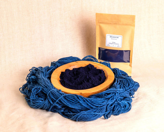 Indigo Dye by Morrow Archival, shown as a deep blue powder in a wooden bowl, with rich indigo-dyed wool yarn and a labeled kraft pouch. Sourced from Indigofera tinctoria, this legendary plant-based dye has been used for millennia across Asia, Africa, and the Americas to produce vibrant, lightfast blues. Ideal for vat dyeing, shibori, natural textiles, and artists seeking authentic, sustainable, and historically significant botanical color.