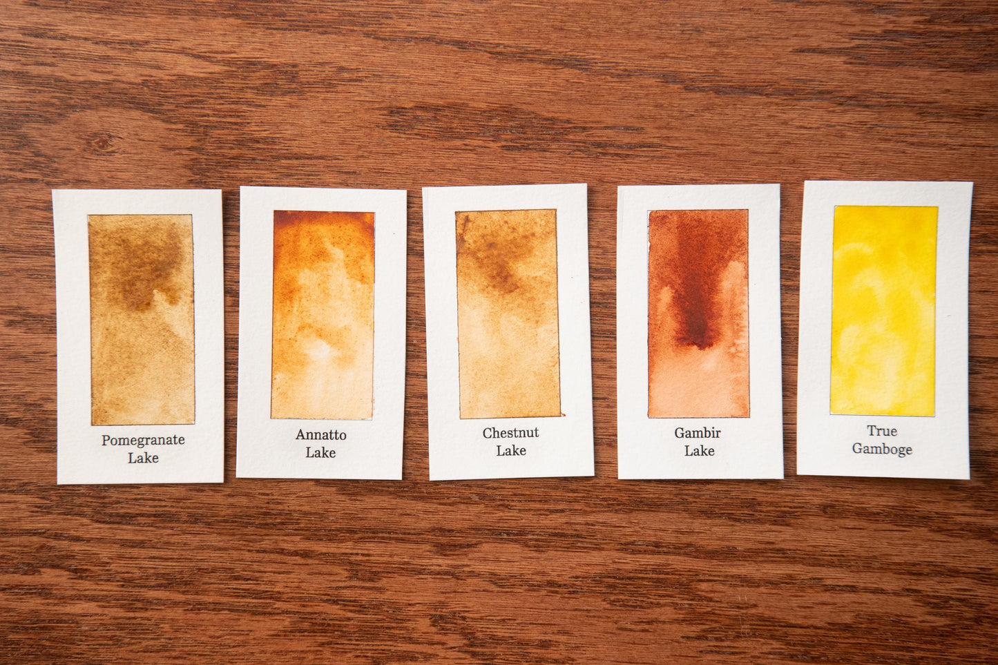 five watercolor paintings with different color variations, arranged on a wooden surface.
