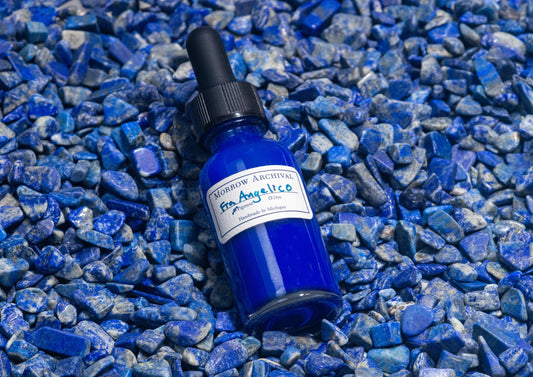 Clear glass bottle of Fra Angelico Blue ink nestled on raw lapis lazuli stones, showing the mineral‚Äôs ultramarine blue veins. The iconic semi-precious stone underscores the historic and luxurious origin of this deep celestial pigment.