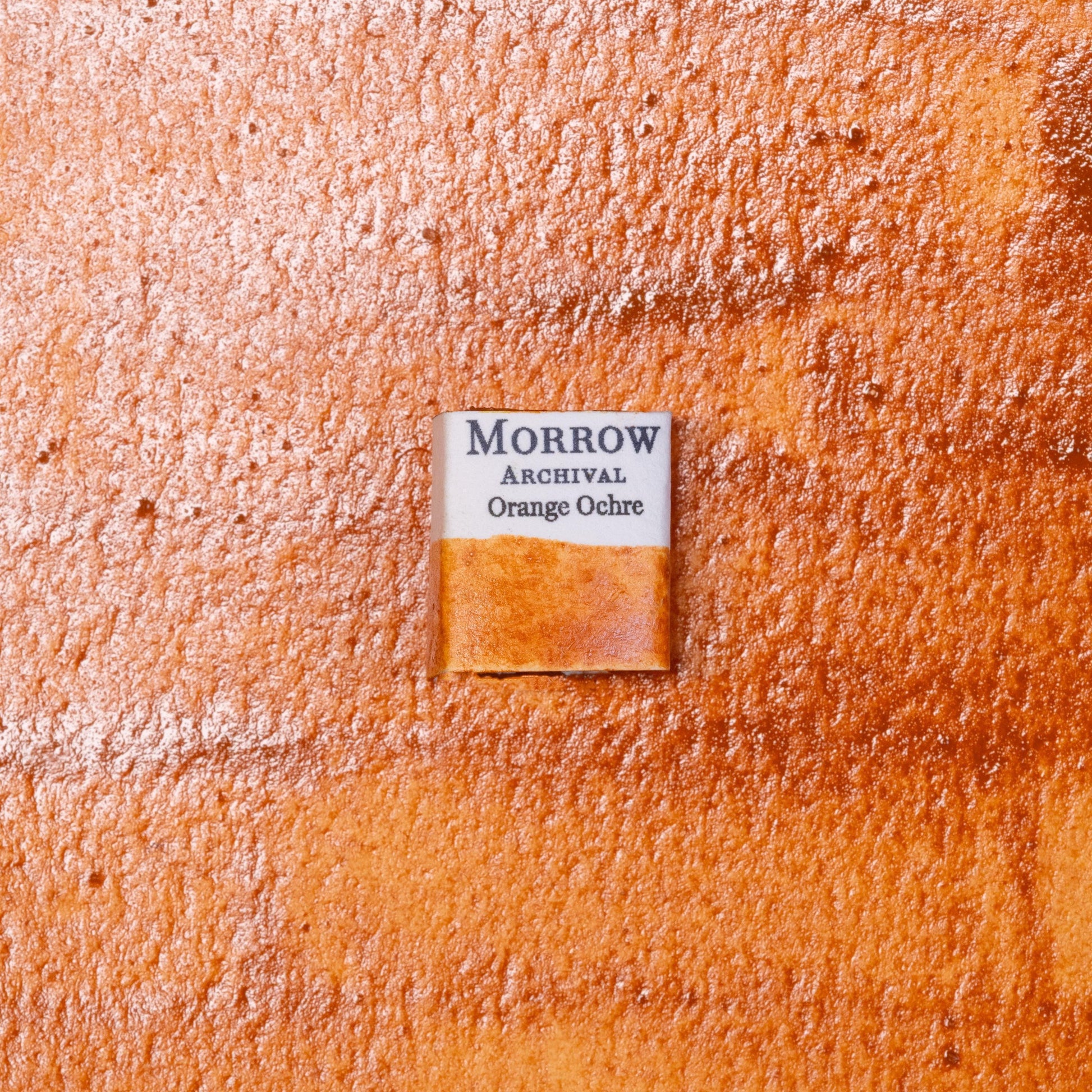 Close-up image of a half pan of Orange Ochre handmade watercolor paint, showing a warm, earthy orange with a matte finish and gentle granulation. The pan rests on a neutral or rustic background, highlighting the pigment‚Äôs natural origin and hand-crafted quality. Ideal for artists looking for a rich, historic ochre with strong warmth and natural depth.