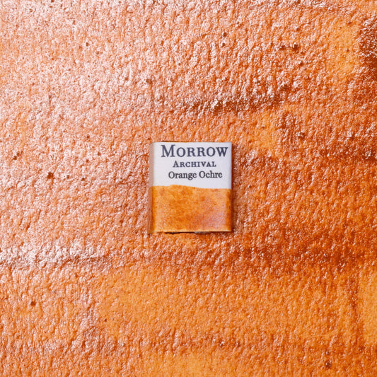 Close-up image of a half pan of Orange Ochre handmade watercolor paint, showing a warm, earthy orange with a matte finish and gentle granulation. The pan rests on a neutral or rustic background, highlighting the pigment‚Äôs natural origin and hand-crafted quality. Ideal for artists looking for a rich, historic ochre with strong warmth and natural depth.
