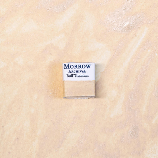 Close-up image of a half pan of Buff Titanium handmade watercolor paint, featuring a soft, warm beige hue with a smooth matte surface. The pan rests on a neutral background, emphasizing the mineral origin and artisanal craftsmanship. Ideal for artists seeking a muted neutral for skin tones, natural landscapes, or desaturated palettes.