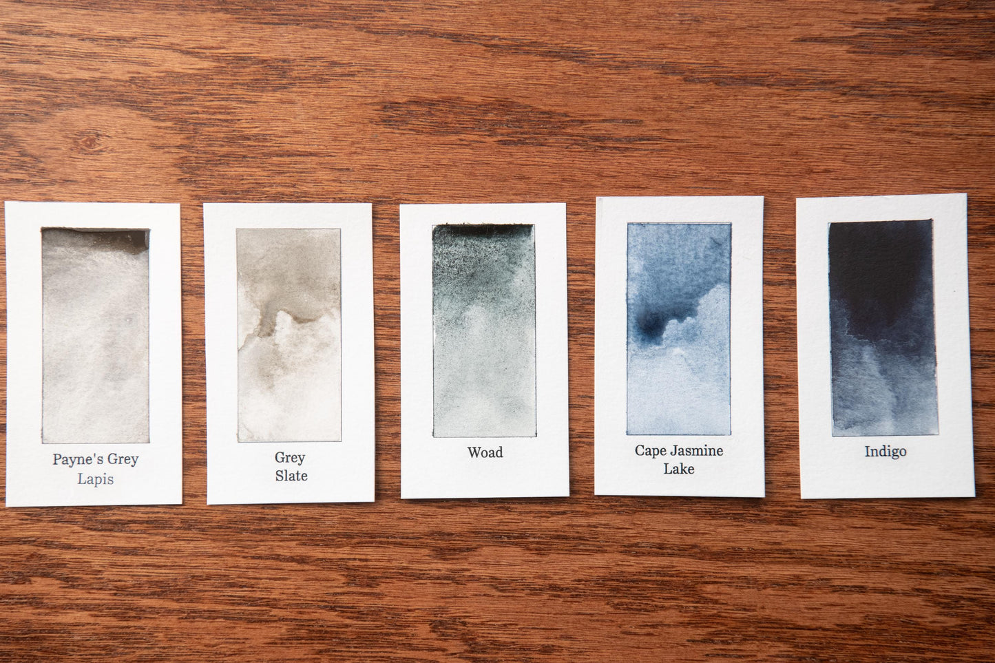 five watercolor paintings with different color variations, arranged on a wooden surface.