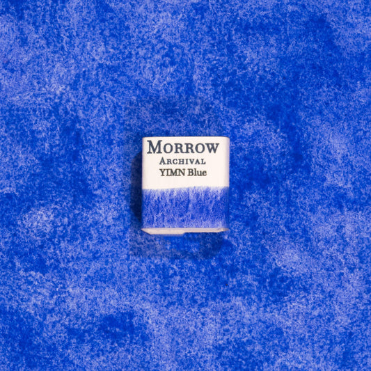 Handmade YInMn Blue natural watercolor paint half pan displayed on a textured watercolor painting. Created from pure single-pigment yttrium, indium, manganese oxide, this vibrant, highly stable blue offers intense color, excellent lightfastness, and smooth granulation, perfect for fine art, historical techniques, and modern illustration. A unique eco-friendly gift for watercolor artists and collectors seeking small-batch, archival-quality, all-natural handmade pigments.