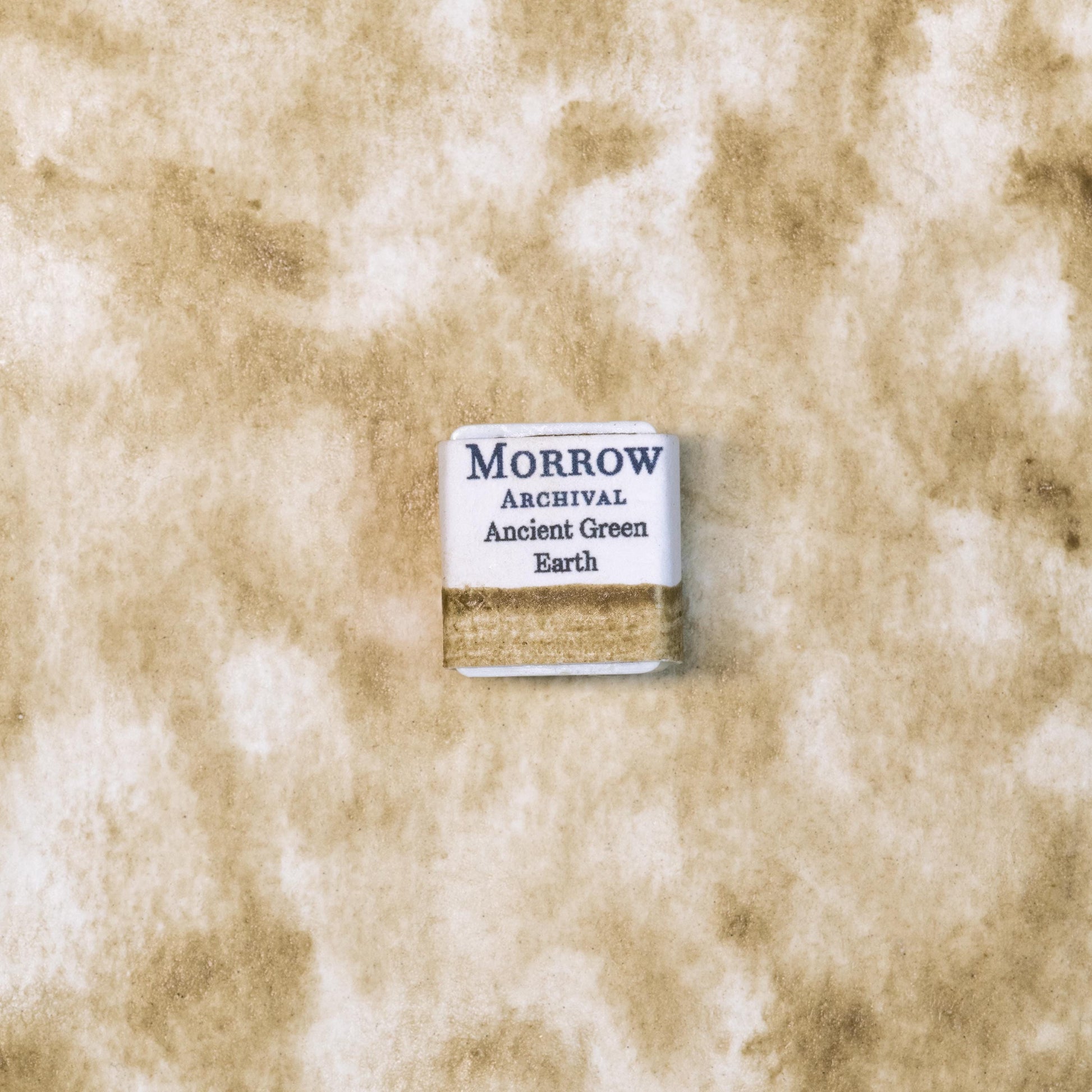 Close-up image of a half pan of Ancient Green Earth handmade watercolor paint, showing a rich, muted green color with a slightly earthy, matte texture. The pan sits on a natural-toned background, emphasizing the artisanal and eco-friendly nature of the product. Perfect for artists seeking natural, non-toxic, high-quality mineral-based watercolor paints.