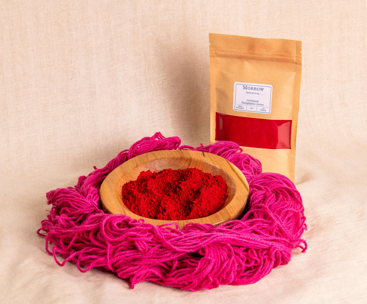 Cochineal Dye by Morrow Archival, shown as a vivid crimson powder in a wooden bowl, with rich pink-to-red dyed wool yarn and a labeled kraft pouch. Made from dried Dactylopius coccus insects, this historic dye yields brilliant scarlets, fuchsias, and purples with exceptional lightfastness. Prized since the Aztec empire and used in European textiles and manuscripts, it’s perfect for natural dyeing, historic art, and eco-conscious fiber crafts.