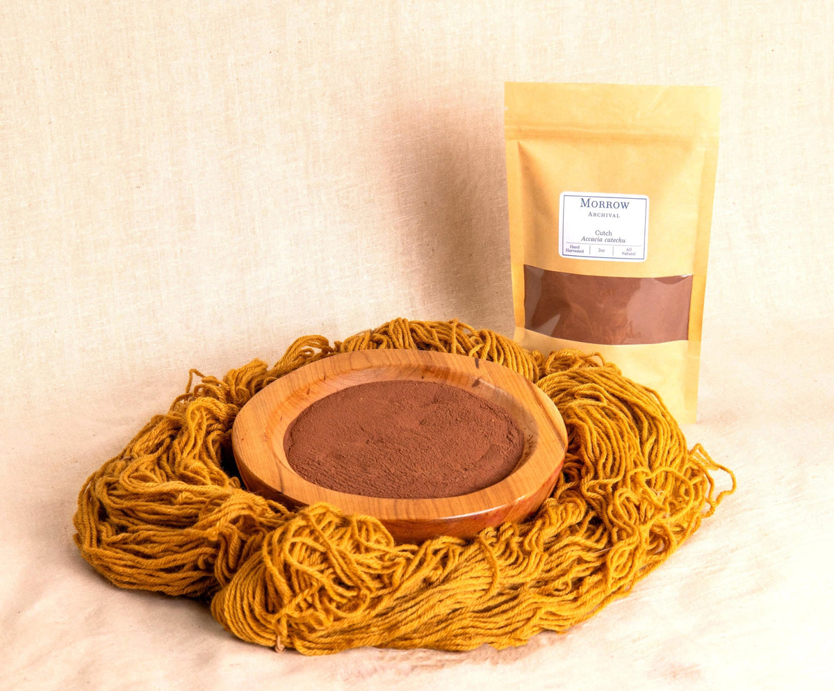 Cutch Dye by Morrow Archival, shown as a warm brown powder in a wooden bowl, with golden brown-dyed wool yarn and a labeled kraft pouch. Extracted from the heartwood of the Acacia catechu tree, this natural dye produces rich tans, chestnuts, and deep browns with excellent lightfastness. Used for centuries in Indian and Southeast Asian textiles, it’s ideal for eco-printing, natural dyeing, and heritage fiber arts with earthy, sustainable color.